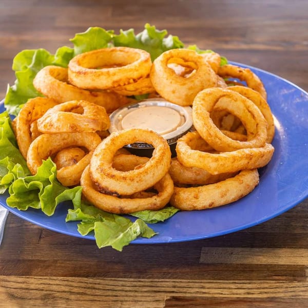 Golden-brown onion rings with two dipping sauces and lettuce on a blue plate.