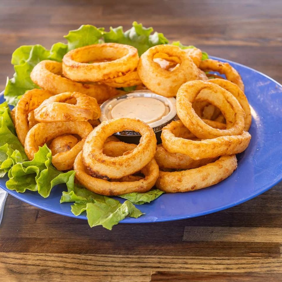 Golden-brown onion rings with two dipping sauces and lettuce on a blue plate.