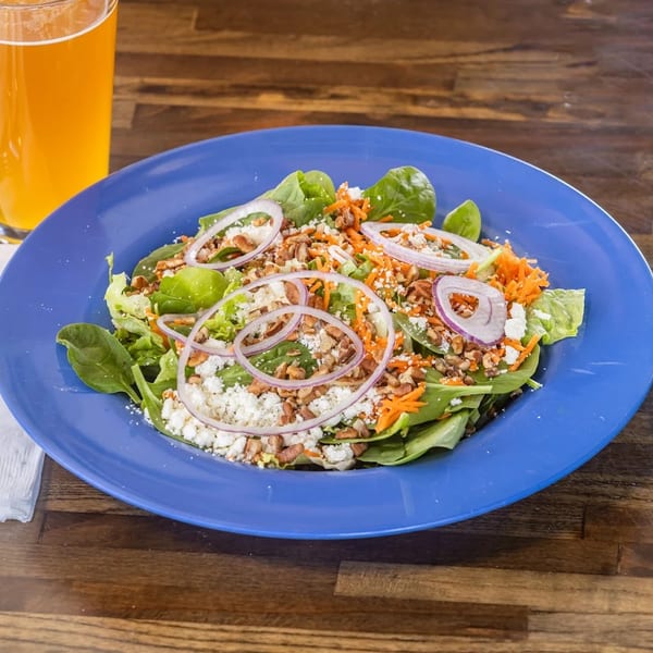 Spinach salad with red onions, shredded carrots, feta cheese, and pecans on a blue plate.