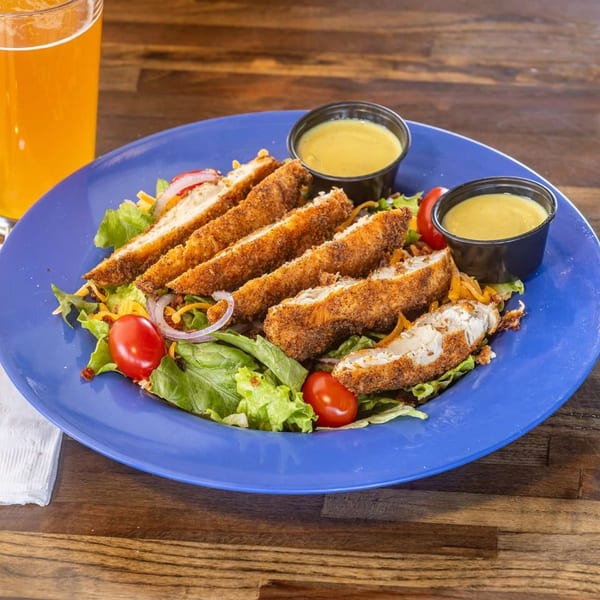 Crispy chicken tender salad with cherry tomatoes, red onion, and two cups of dressing.
