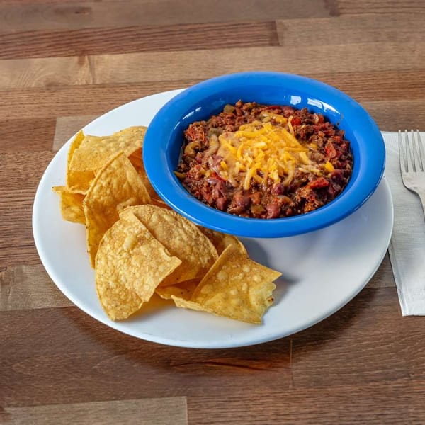 A blue bowl of chili topped with shredded cheese, served with tortilla chips on a white plate.