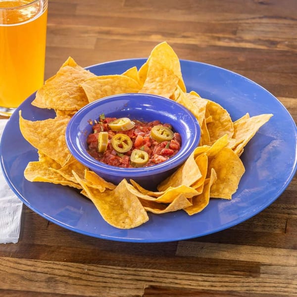 Crispy tortilla chips and salsa with jalapeños on a blue plate, next to a glass of beer.