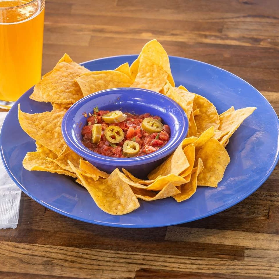 Crispy tortilla chips and salsa with jalapeños on a blue plate, next to a glass of beer.