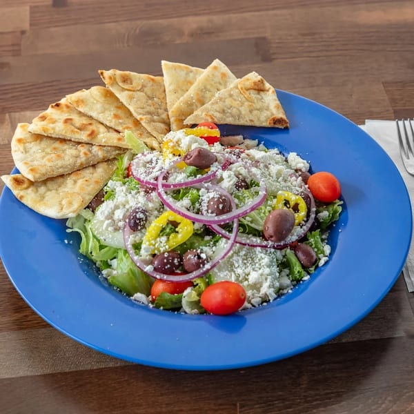 A vibrant Greek salad with feta, olives, tomatoes, and pita bread on a blue plate.