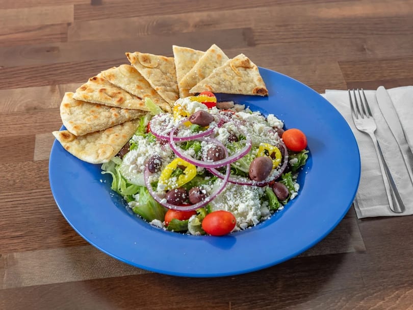 A vibrant Greek salad with feta, olives, tomatoes, and pita bread on a blue plate.